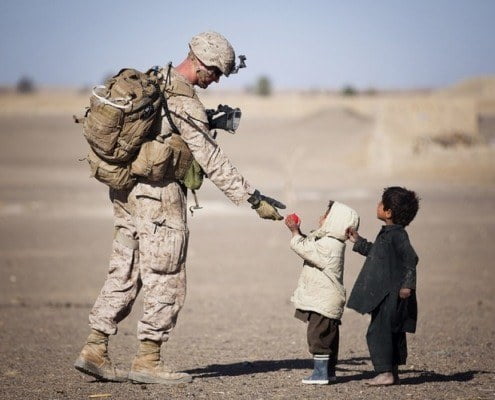 Marine veteran shaking a local child's hand overseas. Veterans are eligible to purchase a home using a VA Loan when they return.